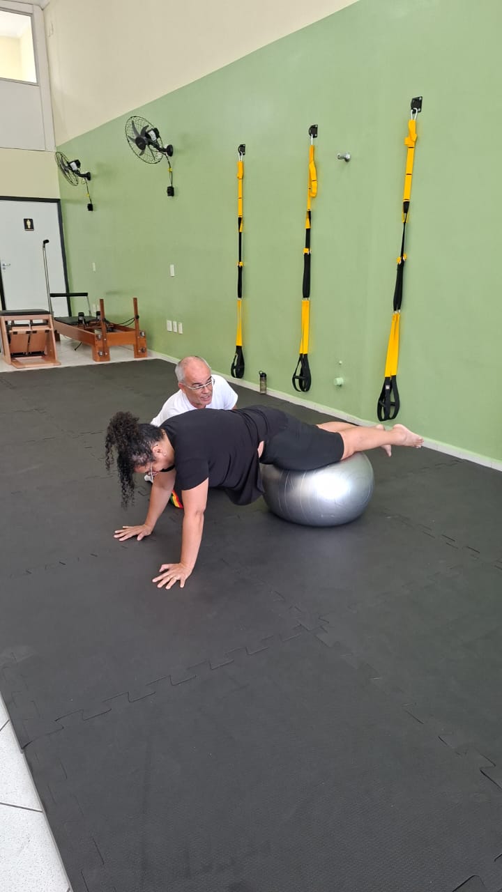 Profissional acompanhando de perto uma aluna durante exercício adaptado
